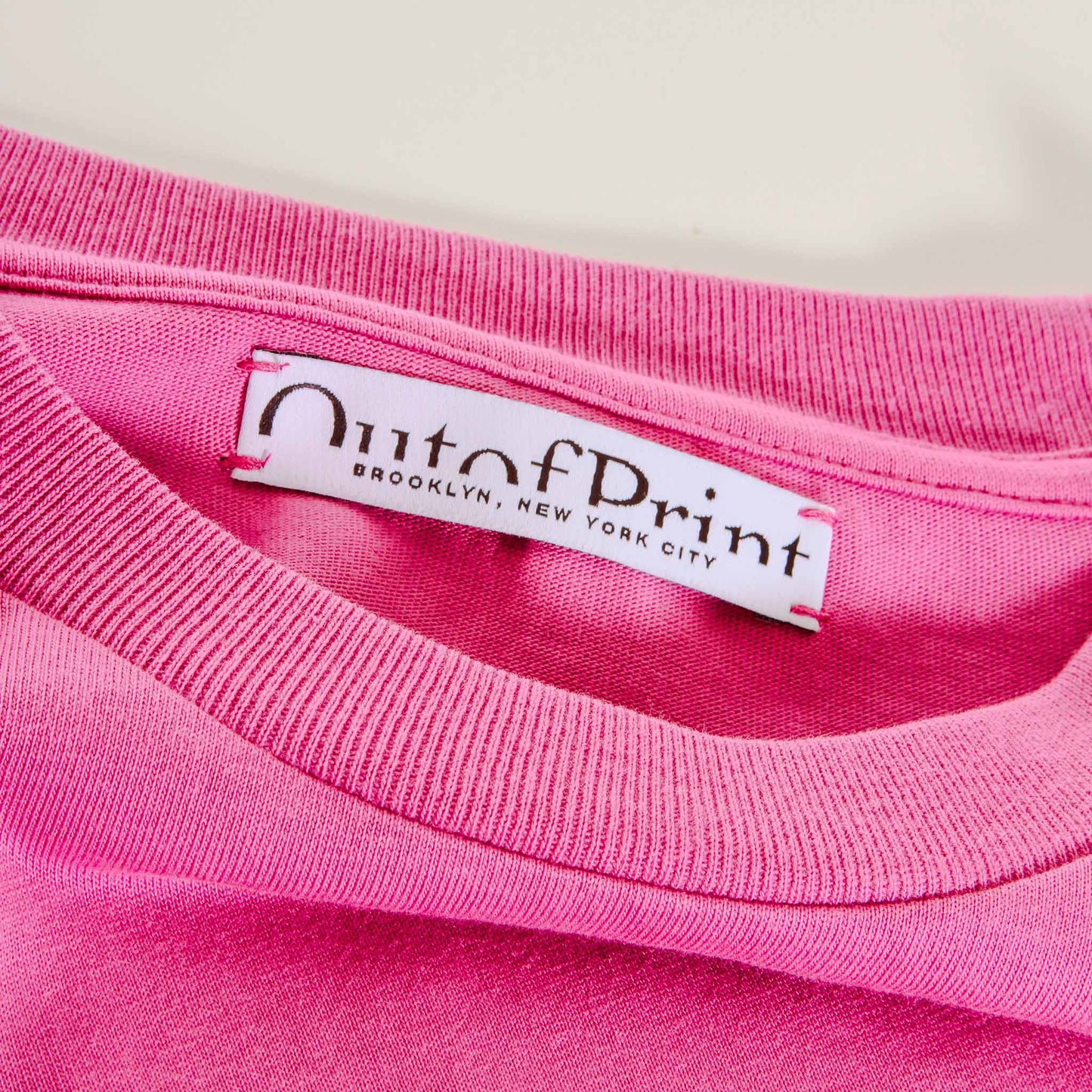 Close-up of a pink garment with 'Out of Print' label on a white background