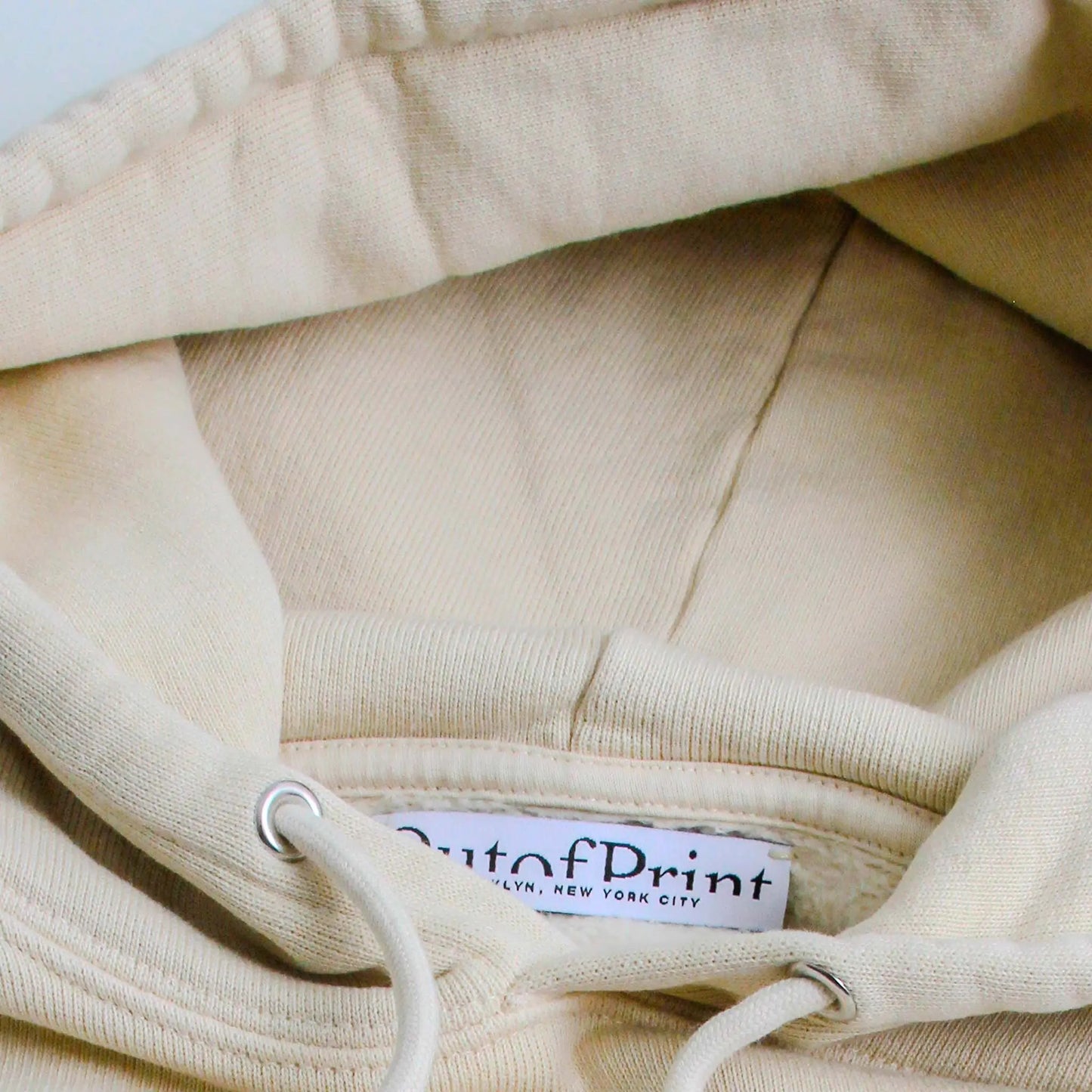 Close-up of a beige hoodie with a brand label on the collar.