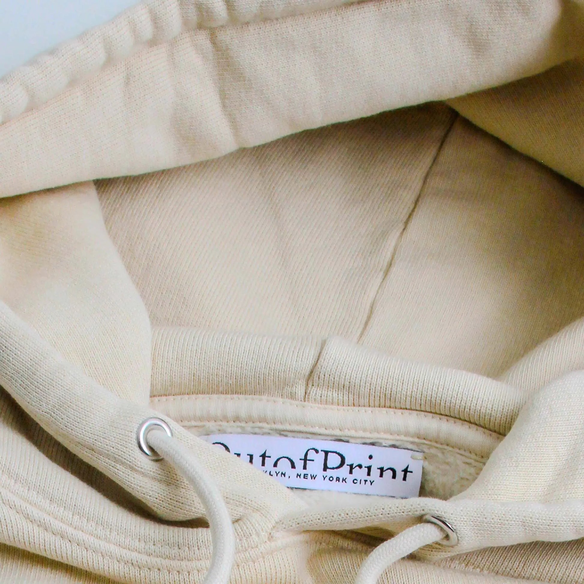 Close-up of a beige hoodie with a brand label on the collar.
