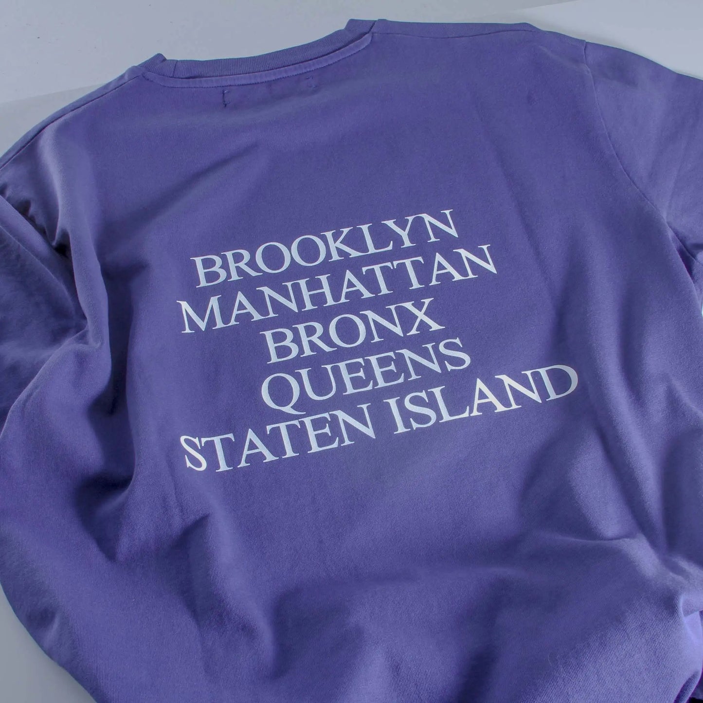 Purple sweatshirt with 'Brooklyn Manhattan Bronx Queens Staten Island' text on a light gray background