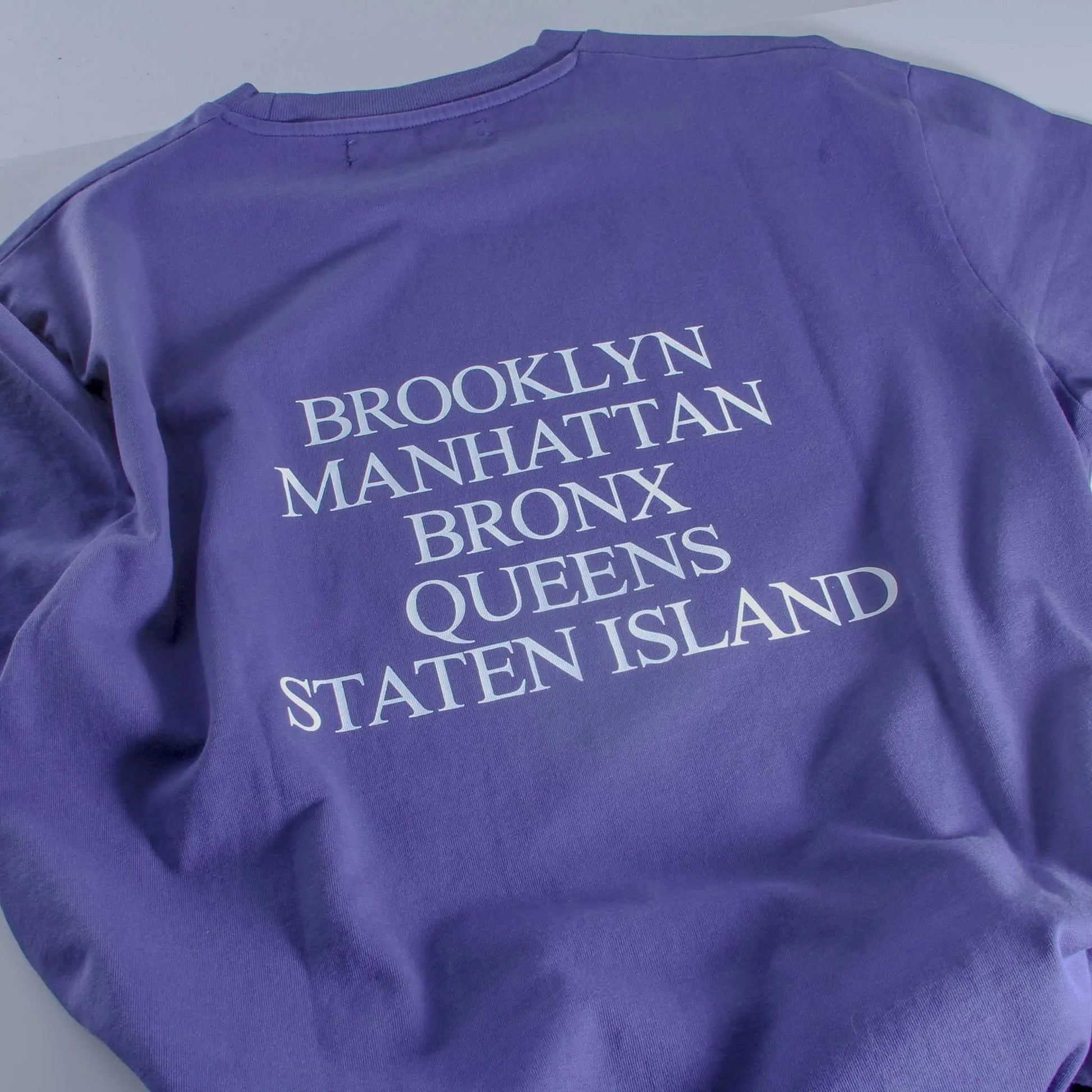 Purple sweatshirt with 'Brooklyn Manhattan Bronx Queens Staten Island' text on a light gray background
