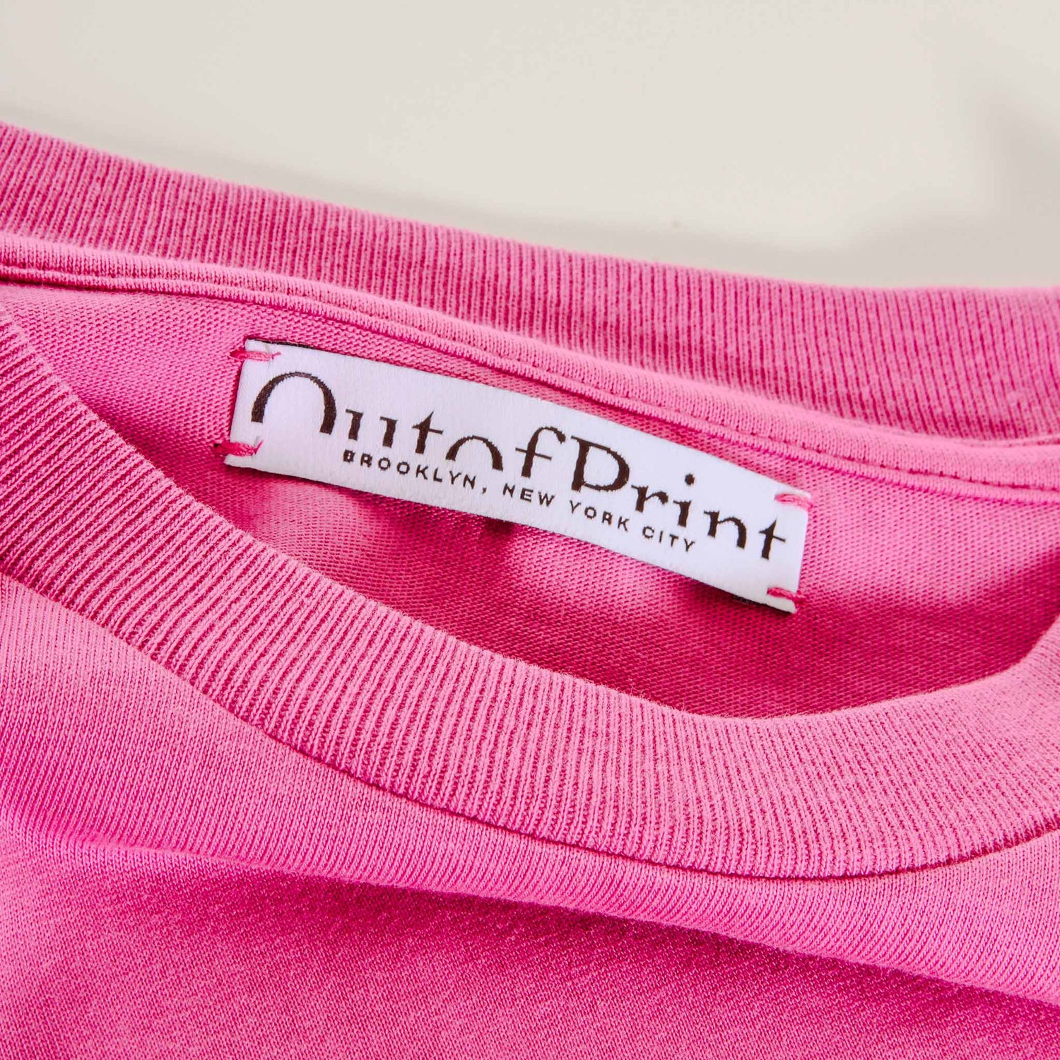 Close-up of a pink garment with 'Out of Print' label on a white background