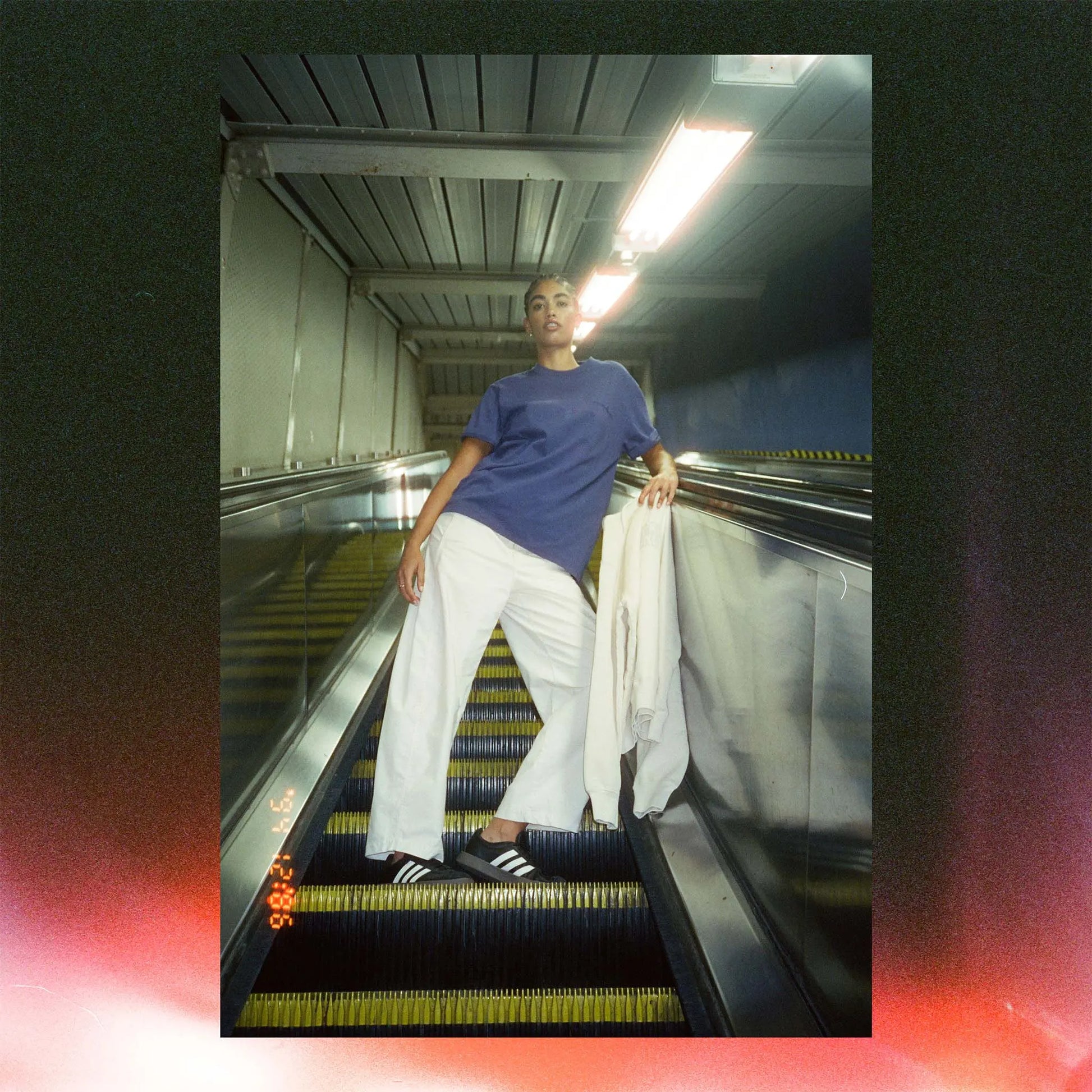 Person in a blue shirt and white pants standing on an escalator with a blurred background